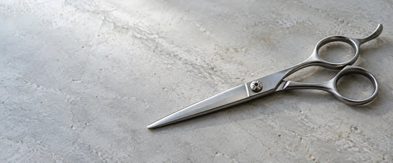 Une paire de ciseaux de coupe posée sur une pierre claire.